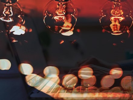 Double exposure image of a woman's hands on a laptop with three light bulbs and lights spots surrounding it.