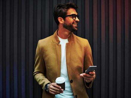 Smiling businessman with smart phone and cup.
