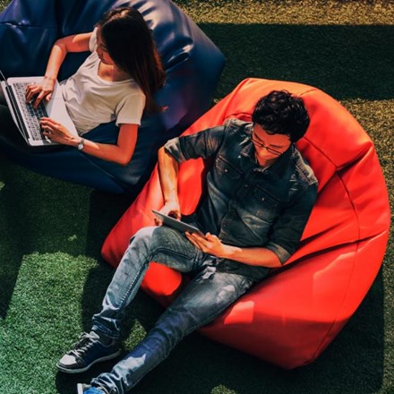 Young Asian couple using laptop notebook and digital tablet together in modern public park, sit on bean bag, top view with copy space on grass.