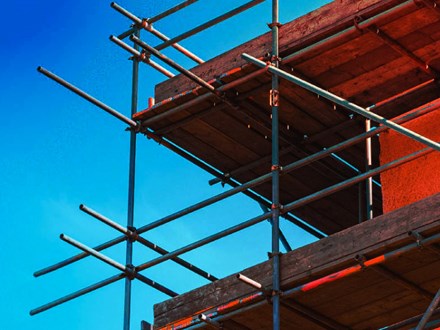 Corner of a home construction with scaffolding against a blue sky.