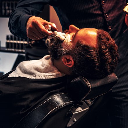 Barber applies shaving foam to a man's face in a saloon.