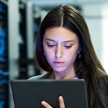 Woman looking at her device while standing next to a data centre. 