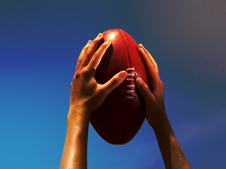 Hands holding Australian football up to the sky