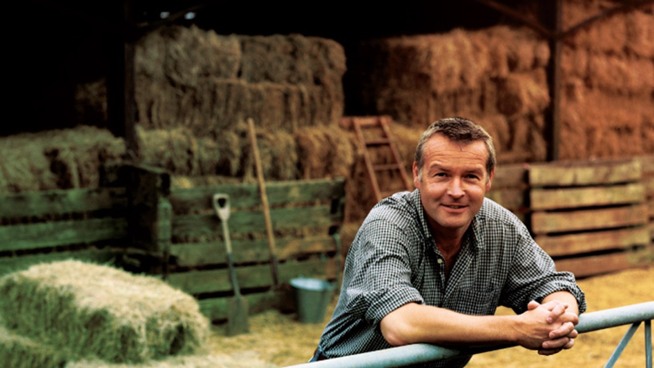 Farmer Leaning on a Gate, With a Barn and Bales of Hay