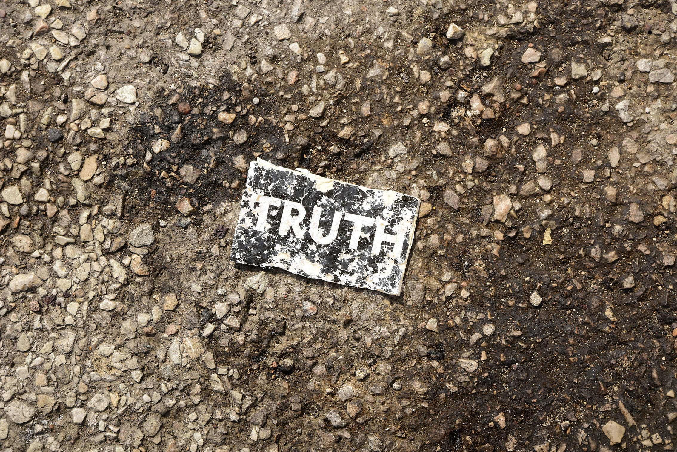 Distressed "TRUTH" sign on a gritty tar surface. 