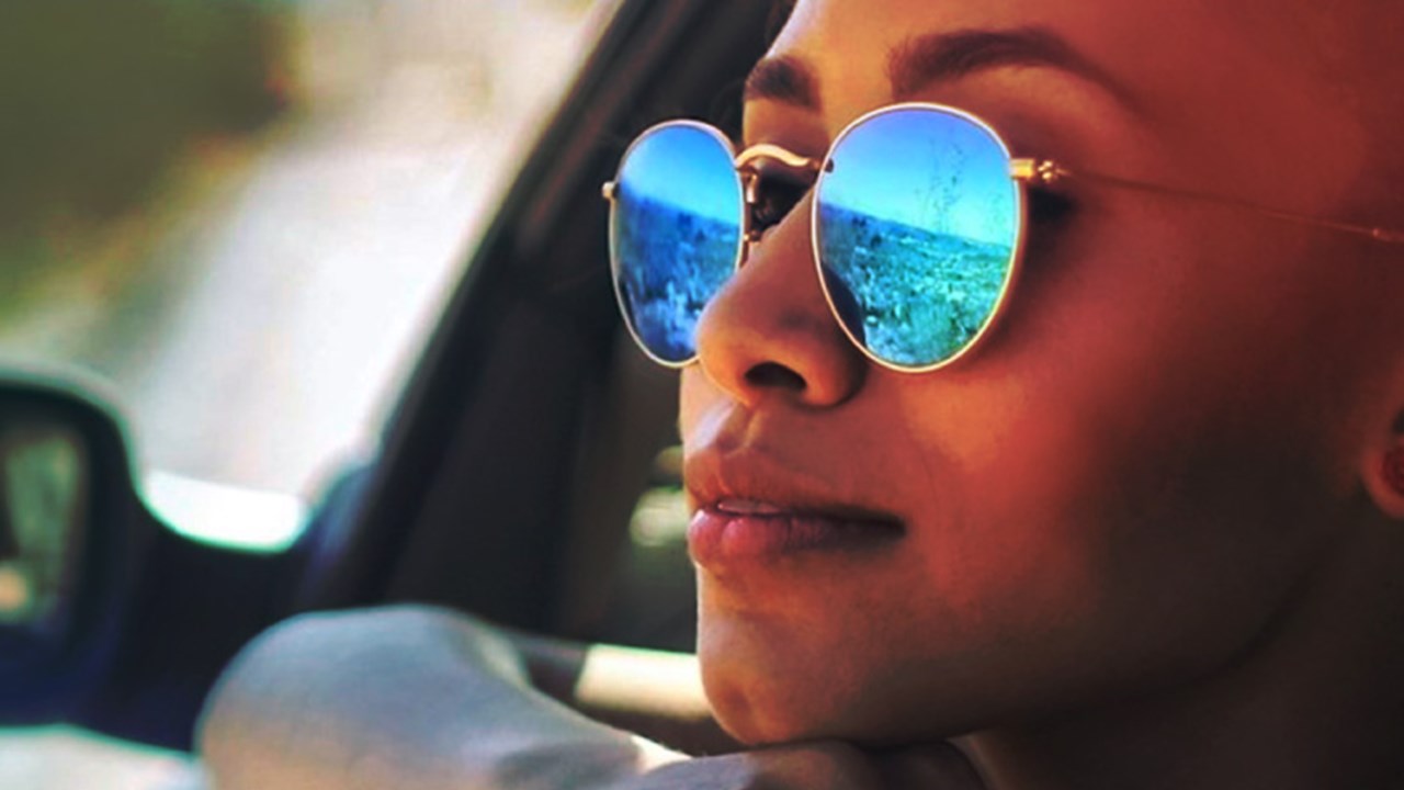 Woman with sunglasses leaning out a car window.