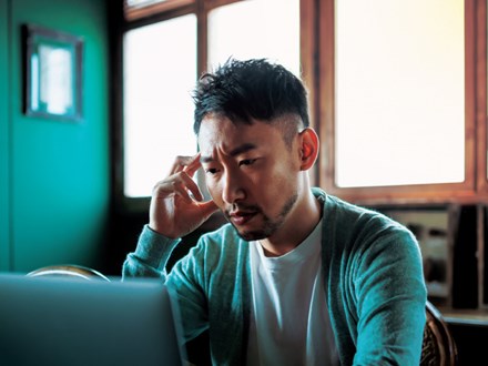Asian man looking perplexed about his finances on a laptop screen